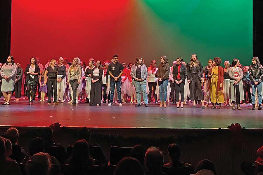 Indoor theater stage full of performers with red, green, and black colored background