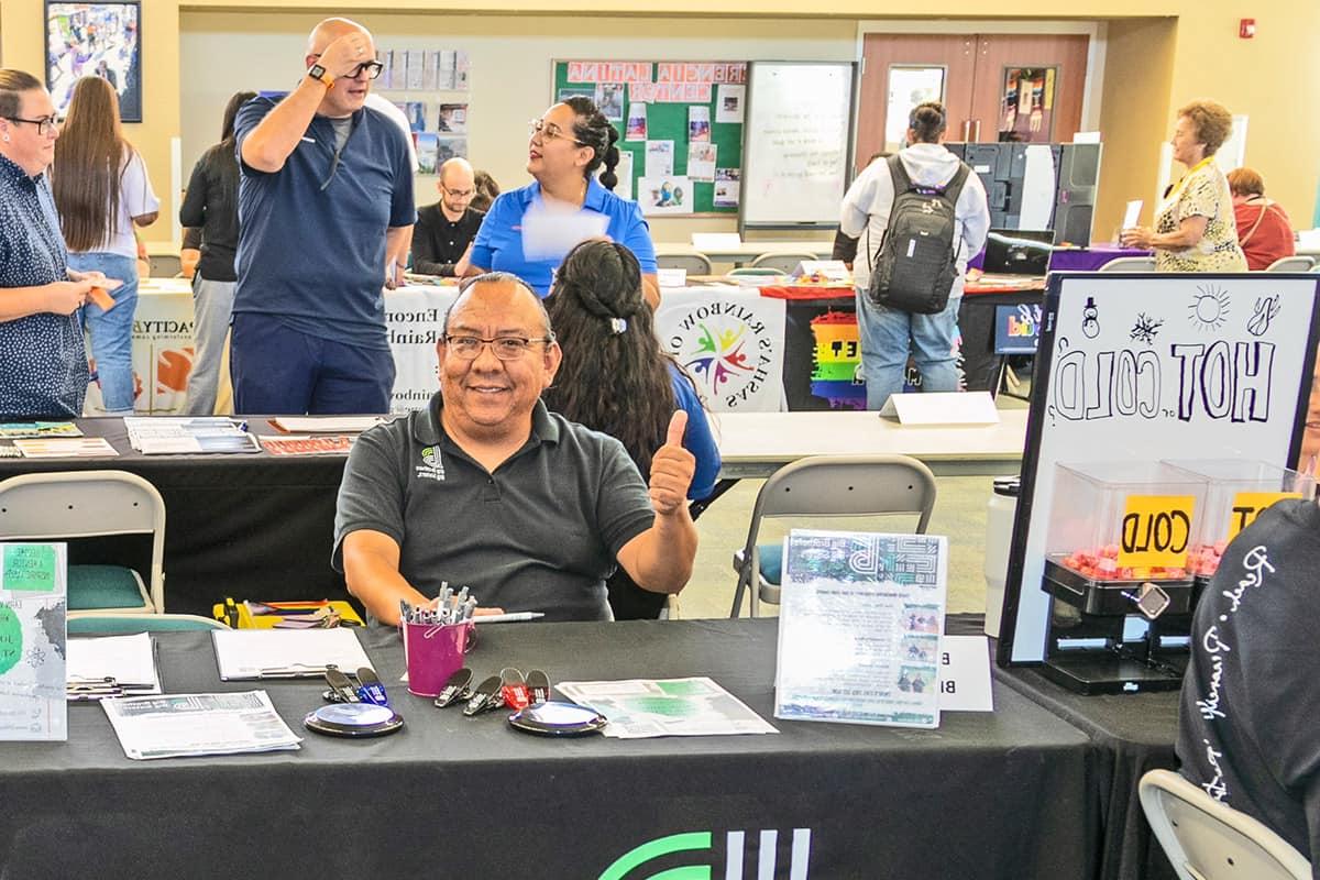 A man smiles a gives a thumbs-up at one of the many employer tables during a community job fair on campus.